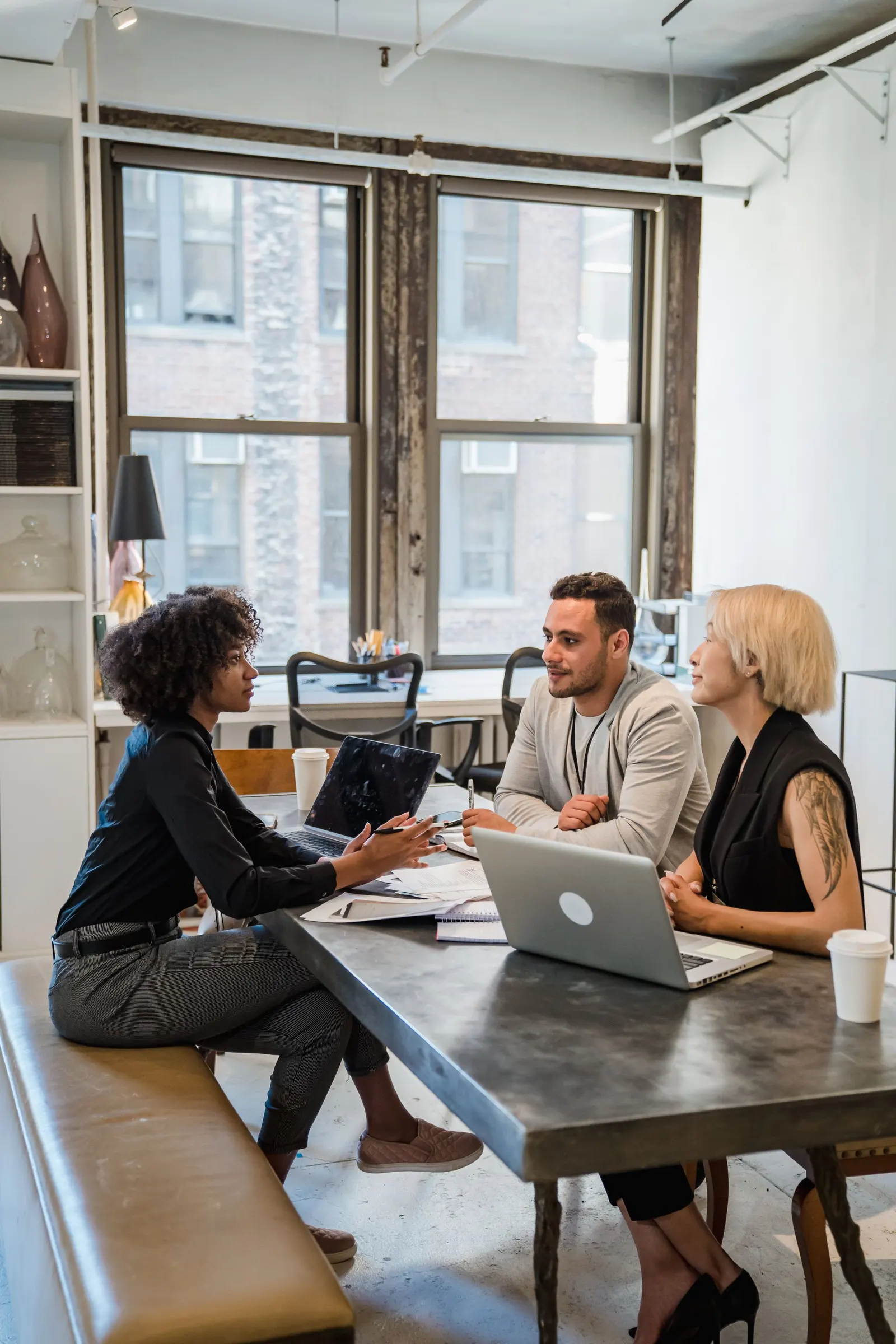 Three colleagues discussing ideas at a desk with laptops in a bright office