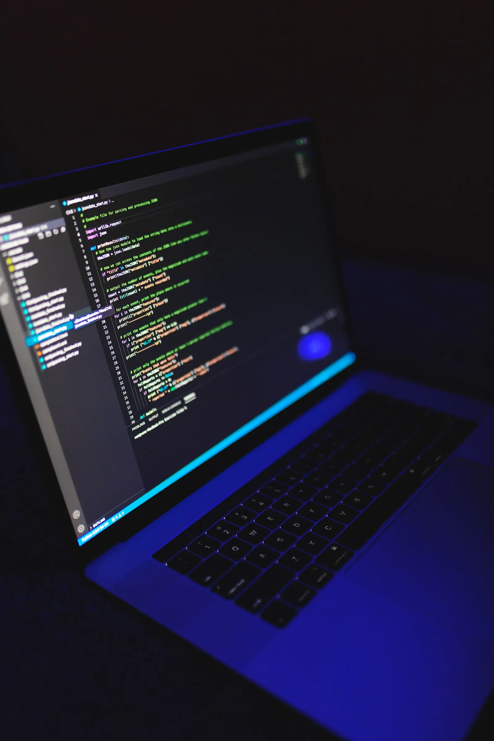 Laptop in a dark room displaying colorful code on screen with blue ambient light