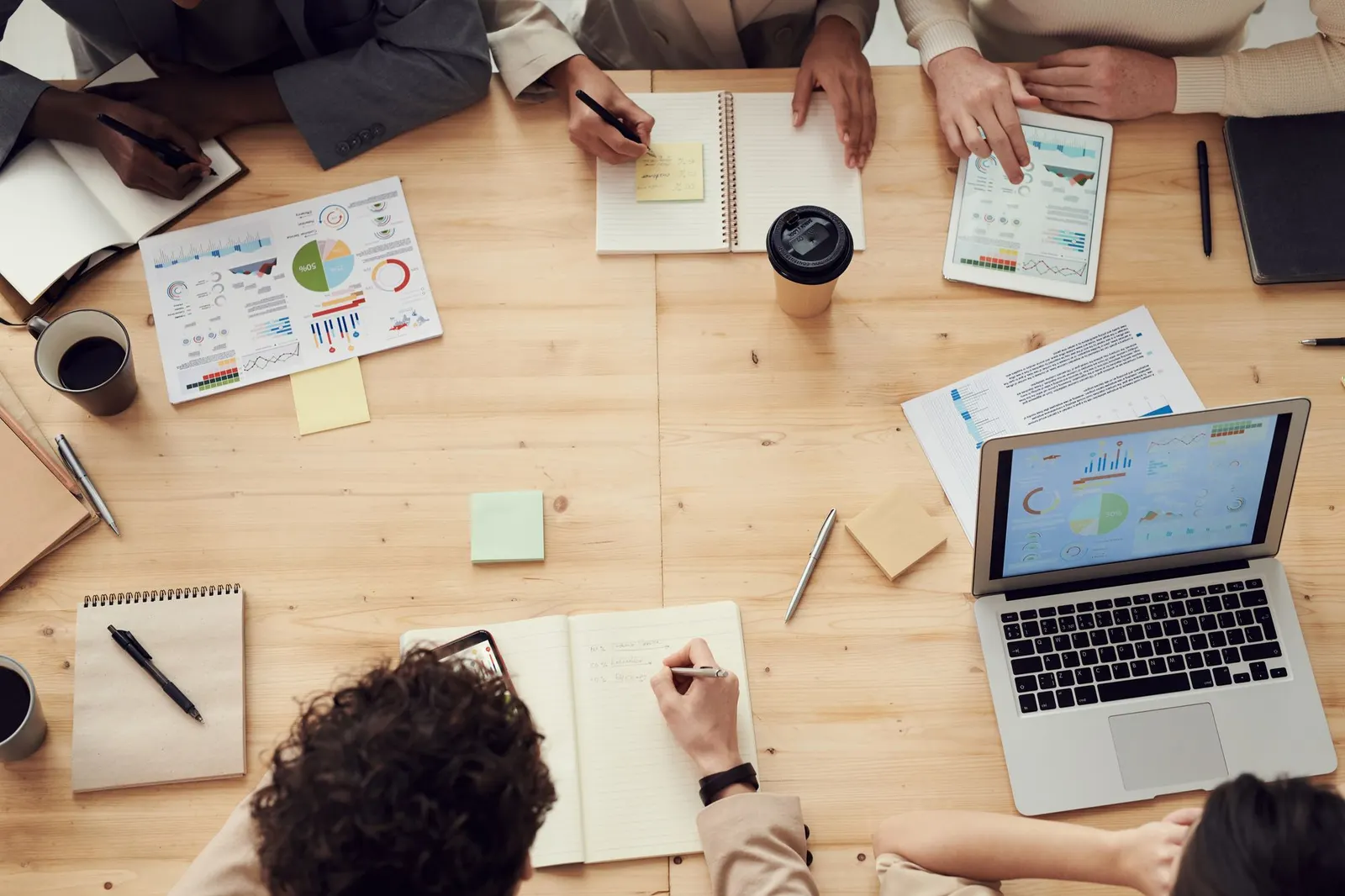 Overhead view of a team around a wooden table with laptops, notebooks and printed charts
