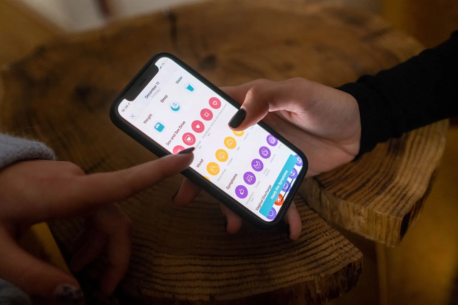Two people tapping colorful icons on a smartphone app screen at a wooden table